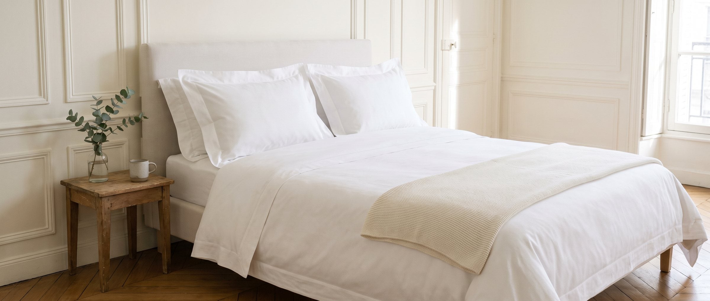 Lit fait de frais avec une taie d’oreiller personnalisée en percale blanche, dans une chambre parisienne